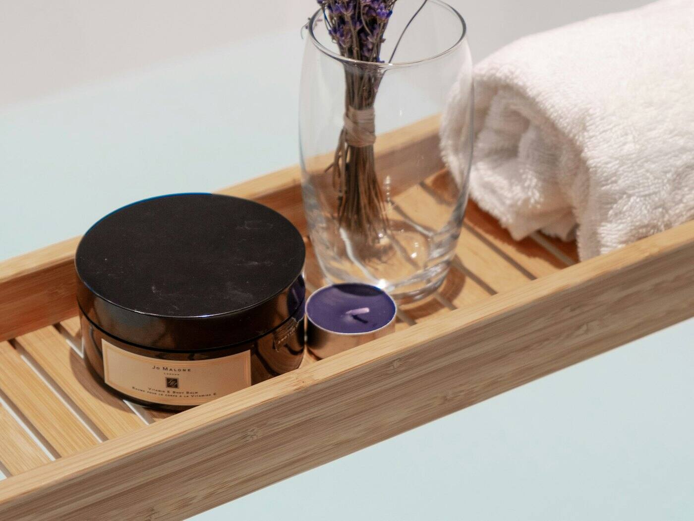 Wooden bath tray with a rolled white towel, a jar of spa product, a small candle, and lavender