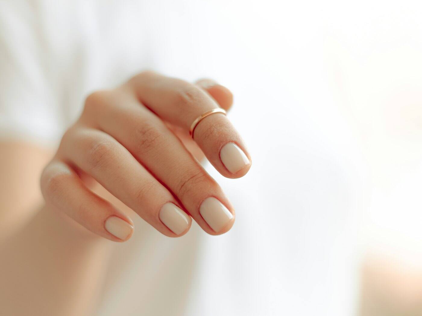 Hand with a white manicure and a thin gold ring against a bright background